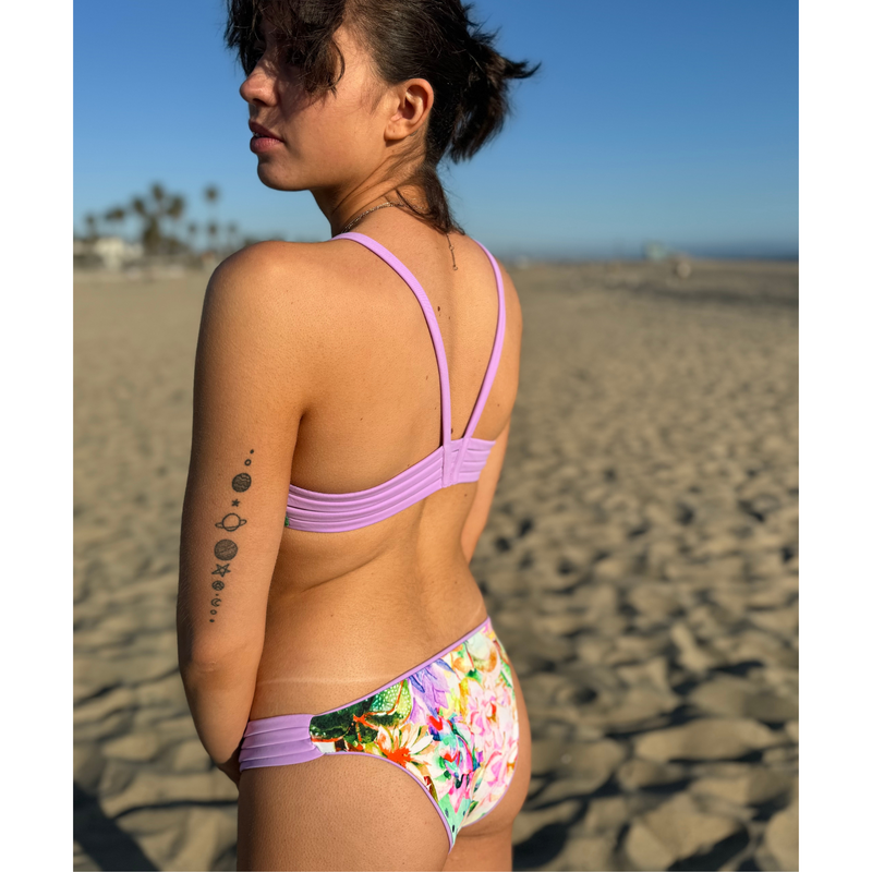 Reversible sport bikini bottom with four strap inserts at hip.  Mid rise with medium back coverage. Solid lilac reverses to a colorful pastel floral print.  Comfortable for sporty athletic girls and women, great for beach volleyball and surfing. Pepper Swimwear.