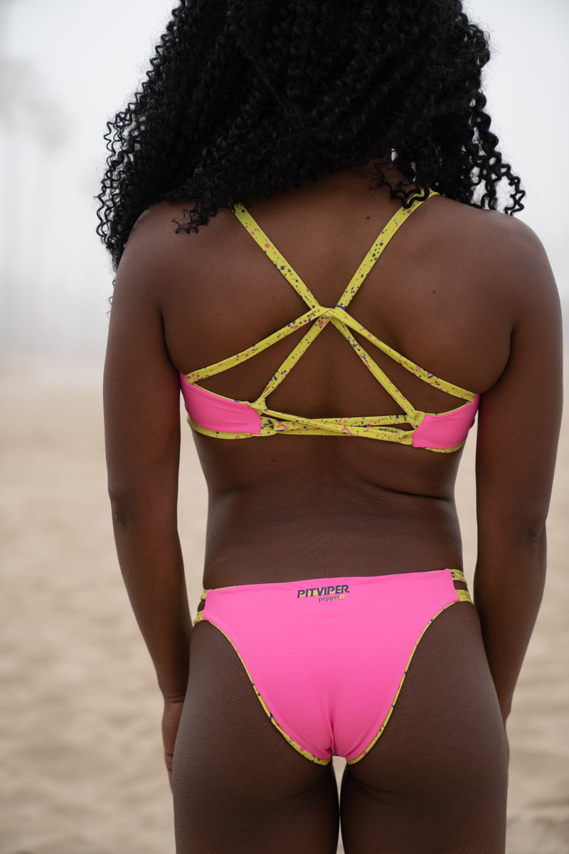 Backview of Pitviper 1993 bikini in pink with lime with purple and pink splatter straps. Reversible to all lime splatter. Criss cross star shaped top back design and cheeky but not too cheeky bottom coverage.